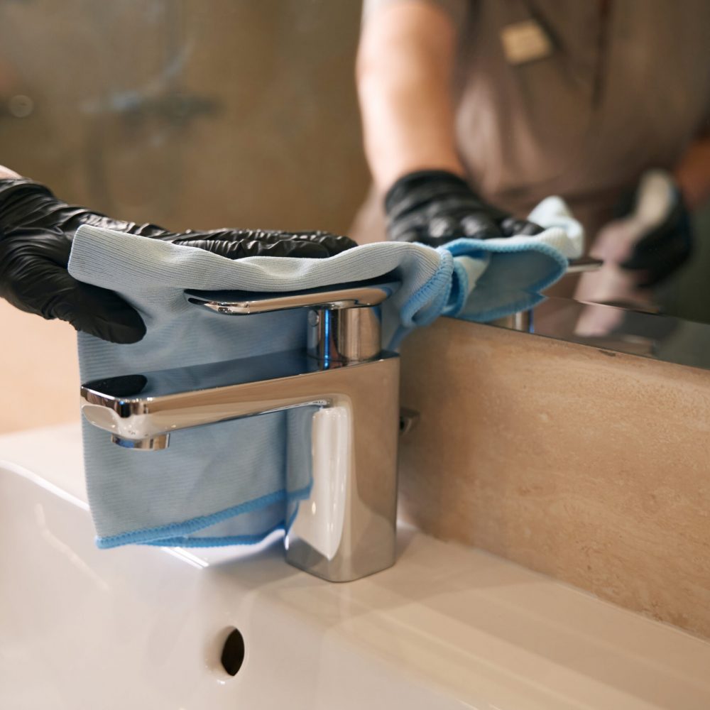 Cropped photo of cleaner in disposable glove wiping tap with microfiber cloth